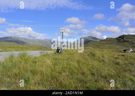 Ein beladenes Tourfahrrad lehnt sich auf einer abgelegenen einspurigen Straße von Nedd, Highland, Schottland, gegen ein Schild mit passender Stelle Stockfoto