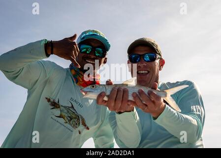 Ambergris Caye, Belize - November, 16, 2019. Aufgeregt Fliegenfischer mit Belizean Fishing Guide zeigt die bonefish, die er gerade in der Karibik gefangen Stockfoto