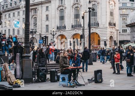 London, Großbritannien - 24 November, 2019: Leute beobachten Gaukler auf der Tastatur spielen und singen auf der Piccadilly Circus, einer der beliebtesten touristischen Gegenden in Lon Stockfoto