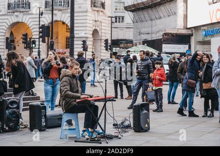 London, Großbritannien - 24 November, 2019: Leute beobachten Gaukler auf der Tastatur spielen und singen auf der Piccadilly Circus, einer der beliebtesten touristischen Gegenden in Lon Stockfoto