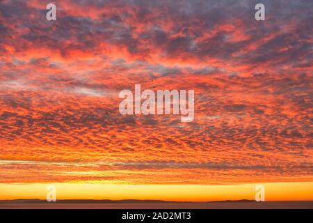 Fiery orange Sonnenaufgang, Sonnenuntergang Himmel mit dramatischen Makrele Wolkenbildung über dem Meer. Stockfoto