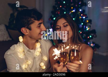 Weihnachten und Neujahr party Konzept. Verliebtes Paar brennende Wunderkerzen beleuchtete Weihnachtsbaum mit Champagner. Stockfoto