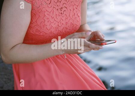 Nicht erkennbare junge Frau sitzt am Wasser mit ihrem Smartphone oder Handy Stockfoto