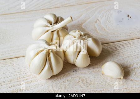 Drei Köpfe von rohem Knoblauch und eine Zehe auf einem weißen Holztisch. Würzig kochen Zutat. Vitamin gesunde Ernährung. Gemüse und Vegetarisch. Ansicht von oben. Stockfoto