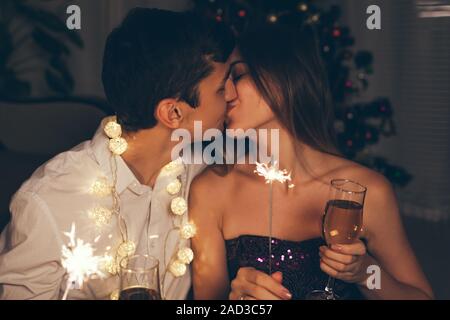 Weihnachten und Neujahr party Konzept. Paar küssen, brennende Wunderkerzen beleuchtete Weihnachtsbaum mit Champagner. Stockfoto