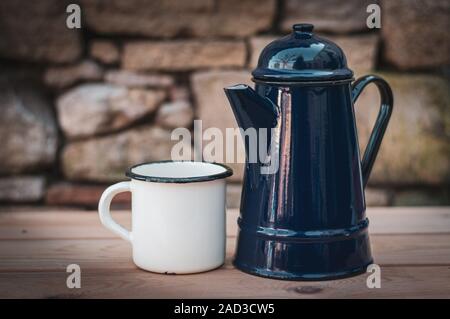 Alte Emaille Tasse und blauen Topf. Draußen auf Holz Tisch gegen die Mauer aus Stein. Stockfoto