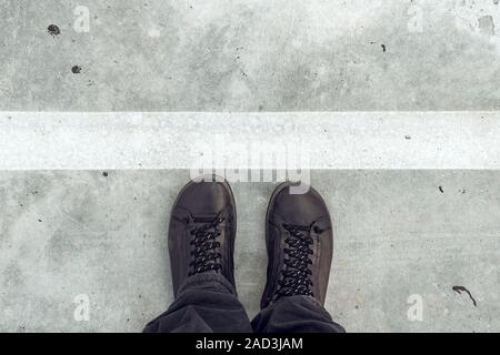 Bei Trennlinie, männliche Füße und Schuhe von oben auf Beton Gehweg mit weißen Linie als Grenze Stockfoto