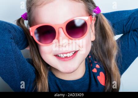 Freundlich lächelnde niedliche Kind mit Zähnen abgefallen - vorschüler Mädchen in der Sonnenbrille mit offenen Mund ohne Milch Zahn Stockfoto