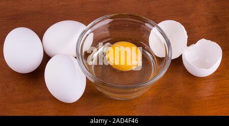 Gebrochene Eier in einer Glasschale mit ganzen Eiern und Shell auf Holz Tisch Stockfoto