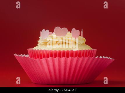 Vanilla Cupcake mit essbaren Herzen auf Vanille Glasur, roter Hintergrund Stockfoto