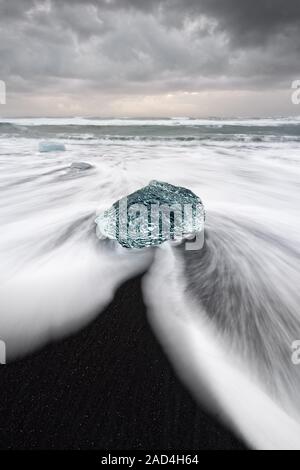 Runde Eisblock in blauen Tönen an einem Strand mit starker Brandung, das Wasser zurückfließt zeigt eine markante und Spuren von Bewegung (langfristige Exposition) Stockfoto