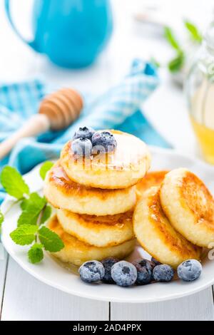 Quark-Pfannkuchen mit Honig und Heidelbeere auf weißem Hintergrund, Frühstück oder Mittagessen Stockfoto