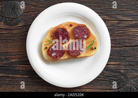 Sandwich mit in Scheiben geschnittenen Salami und geröstetes Brot in der Platte auf Holztisch, Ansicht von oben Stockfoto