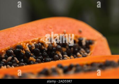 Die Hälfte der reife Papaya mit Samen mit einem grünen Pflanzen für den Hintergrund. Scheiben von sweet Papaya. Halbierte Papaya. Gesunde exotische Früchte. Vegetarisches Essen. Stockfoto
