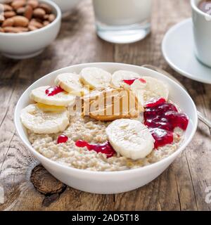 Gesundes Frühstück am Morgen - Haferflocken mit Scheiben von Bananen, himbeermarmelade und Erdnussbutter. Von der Seite. Stockfoto