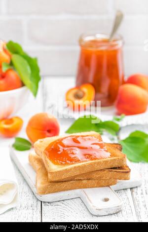 Toast Brot mit Marillenmarmelade und frisches Obst mit Blättern auf weißer Holztisch. Leckeres Frühstück. Stockfoto