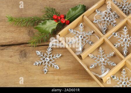 Jeweled Schneeflocke Weihnachtsschmuck in einem Kasten mit Holly und Tannennadeln auf rustikalem Holz Stockfoto