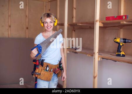 Handliche Frau mit kurzen Haaren mit Kopfhörer arbeitet mit Säge, versuchen es zu Licks. Stockfoto