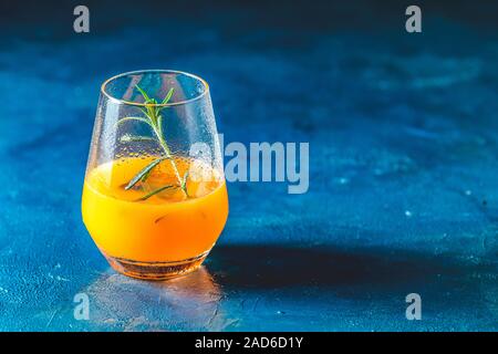 Gelb Orange Cocktail mit Mandarine und Rosmarin in Glas auf dunkelblau konkreten Hintergrund, aus der Nähe. Weihnachten und Neujahr Urlaub Welcome Drink. Stockfoto