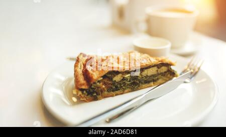 Spinat und Chicken Pie, Zwiebel und Ei. aromatischer Kaffee auf einem Marmortisch in einem Cafe, Sonnenuntergang Licht vom Fenster Stockfoto