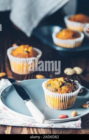 Vanille Karamell Muffins in Papier Becher und Flaschen von Milch auf dunklem Hintergrund. Köstliche Kuchen mit Rosinen, Mandeln und Nüsse. Hausgemachte biscui Stockfoto