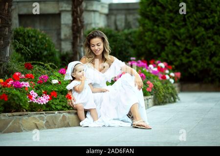 Schöne junge Mama sitzt mit ihrer Tochter in den Park. Weiße Kleider. Sie sind glücklich und Lachen. Schönes warmes Wetter. Stockfoto