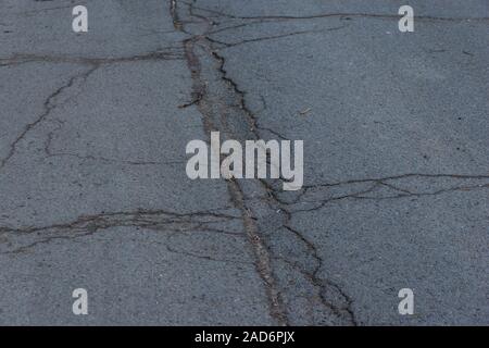 Asphalt Fahrbahn mit kleinen Rissen und Schäden. Bürgersteig Asphaltstraße mit Rissen. Stock. Textur der Asphaltstraße mit Rissen. Zusammenfassung Hintergrund Stockfoto