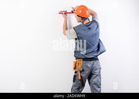 Ein Bauherr in einem Helm, mit Silikon in die Pistole, zielt auf den Rahmen. Stockfoto