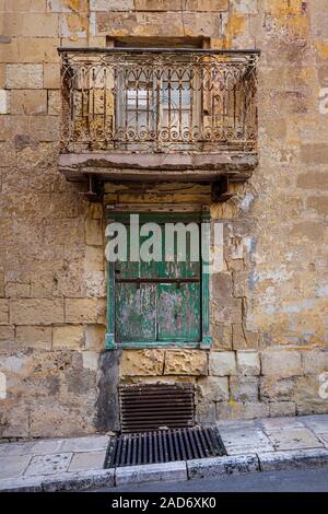 Eine sehr alte traditionelle maltesische Balkon mit rosten aber reich verzierten Balkon Rampe oberhalb einer grün gestrichenen Fensterläden und vergitterten Fenster in Valletta, Malta. Stockfoto