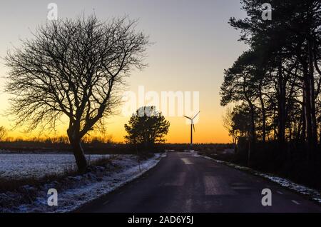 Wind Generator durch eine Landstraße mit Silhouettiert tress in der Wintersaison Stockfoto