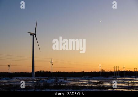 Mühle und Stromleitungen durch Sonnenuntergang in einer Ebene Landschaft durch den Winter Stockfoto