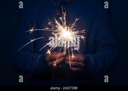 Single Mann in grauen gestrickten Pullover und Lametta um den Hals holding Wunderkerze in nachts dunkel Stockfoto