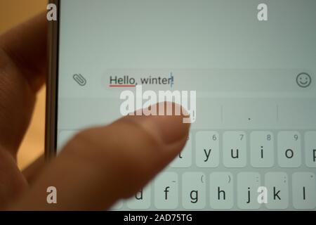 Weibliche hand Tippen auf einen weißen Smartphone eine Nachricht Hallo, Winter. Stockfoto