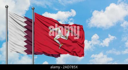 Katar und Isle Of Man Flagge im Wind gegen Weiße bewölkt blauer Himmel zusammen. Diplomatie Konzept, internationale Beziehungen. Stockfoto