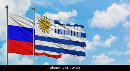 Russland und Uruguay Flagge im Wind gegen Weiße bewölkt blauer Himmel zusammen. Diplomatie Konzept, internationale Beziehungen. Stockfoto