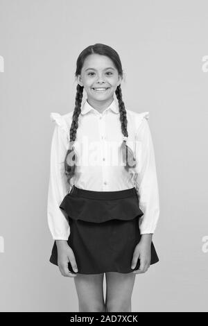 Smart cutie. Süße kleine Mädchen lächelnd auf gelben Hintergrund. Gerne kleine Mädchen tragen Schuluniform. Grundschule Mädchen mit geflochtenem Haar in langen Zöpfen. Adorable girl Stolz, ein Schüler. Stockfoto