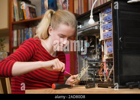 Happy Teenager mit einem Schraubendreher auf einer Erweiterungskarte Leiterplatte aus einem offenen PC während der Durchführung von Reparaturen an den Computer an. Stockfoto