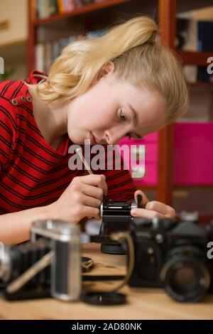 Hohen Schuss ein junges Mädchen mit einem kleinen Schraubendreher eine antike Film Kamera zu reparieren. Weitere Kameras sind unscharf im Vordergrund. Stockfoto