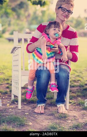 Mutter und süsse kleine Tochter sitzen auf holzbank Stockfoto