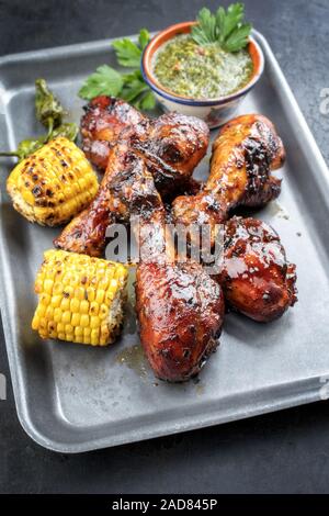 Traditionelle Grill Chicken Drumsticks mit Mais und chimichurri Sauce als Draufsicht in einem silber Fritteuse Stockfoto