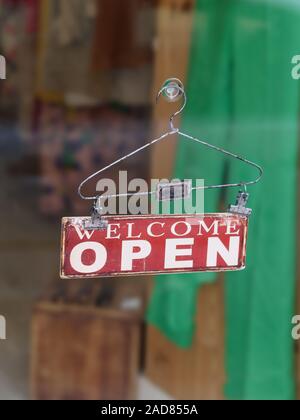 Close-up Willkommen"-Schild hängt an einem Bügel am Eingang Glas Fenster/Tür eines Bekleidungsgeschäfts. Stockfoto