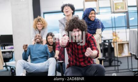 Multiethnics Business Team Racing auf Bürostühle Stockfoto