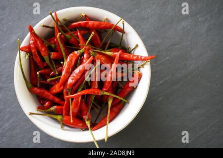 Nahaufnahme einer weißen Schüssel gefüllt mit leuchtend roten Chilies mit grünen Stengeln auf grauem Schiefer Hintergrund mit Kopie Raum; Essen und Kochen Stockfoto