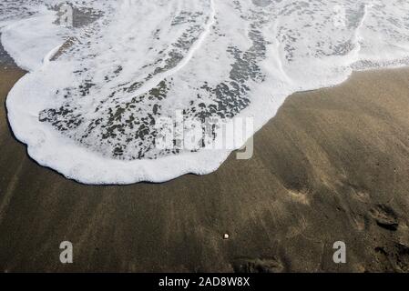 Schöne weiche Welle auf schwarzem Sand am Meer, sonnigen Tag. Stockfoto