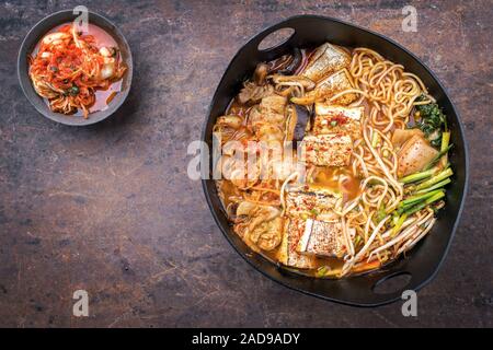 Traditionelles koreanisches Kimchi jjigae mit gegrillter Schweinebauch und Ramen als Draufsicht in modernem Design Japanische gusseiserne Rösten di Stockfoto