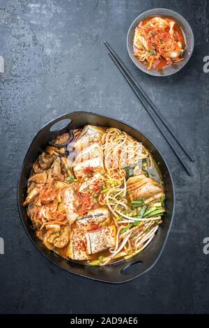 Traditionelles koreanisches Kimchi jjigae mit gegrillter Schweinebauch und Ramen als closeup in modernem Design Japanische gusseiserne Rösten dis Stockfoto