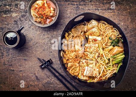 Traditionelles koreanisches Kimchi jjigae mit gegrillter Schweinebauch und Ramen als Draufsicht in modernem Design Japanische gusseiserne Rösten di Stockfoto