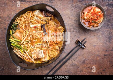 Traditionelles koreanisches Kimchi jjigae mit gegrillter Schweinebauch und Ramen als Draufsicht in modernem Design Japanische gusseiserne Rösten di Stockfoto