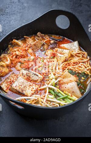 Traditionelles koreanisches Kimchi jjigae mit gegrillter Schweinebauch und Ramen als closeup in modernem Design Japanische gusseiserne Rösten dis Stockfoto