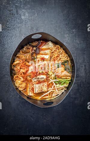 Traditionelles koreanisches Kimchi jjigae mit gegrillter Schweinebauch und Ramen als closeup in modernem Design Japanische gusseiserne Rösten dis Stockfoto